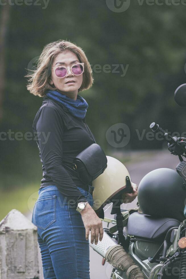 pretty woman holding safety helmet standing beside  small enduro motorcycle photo