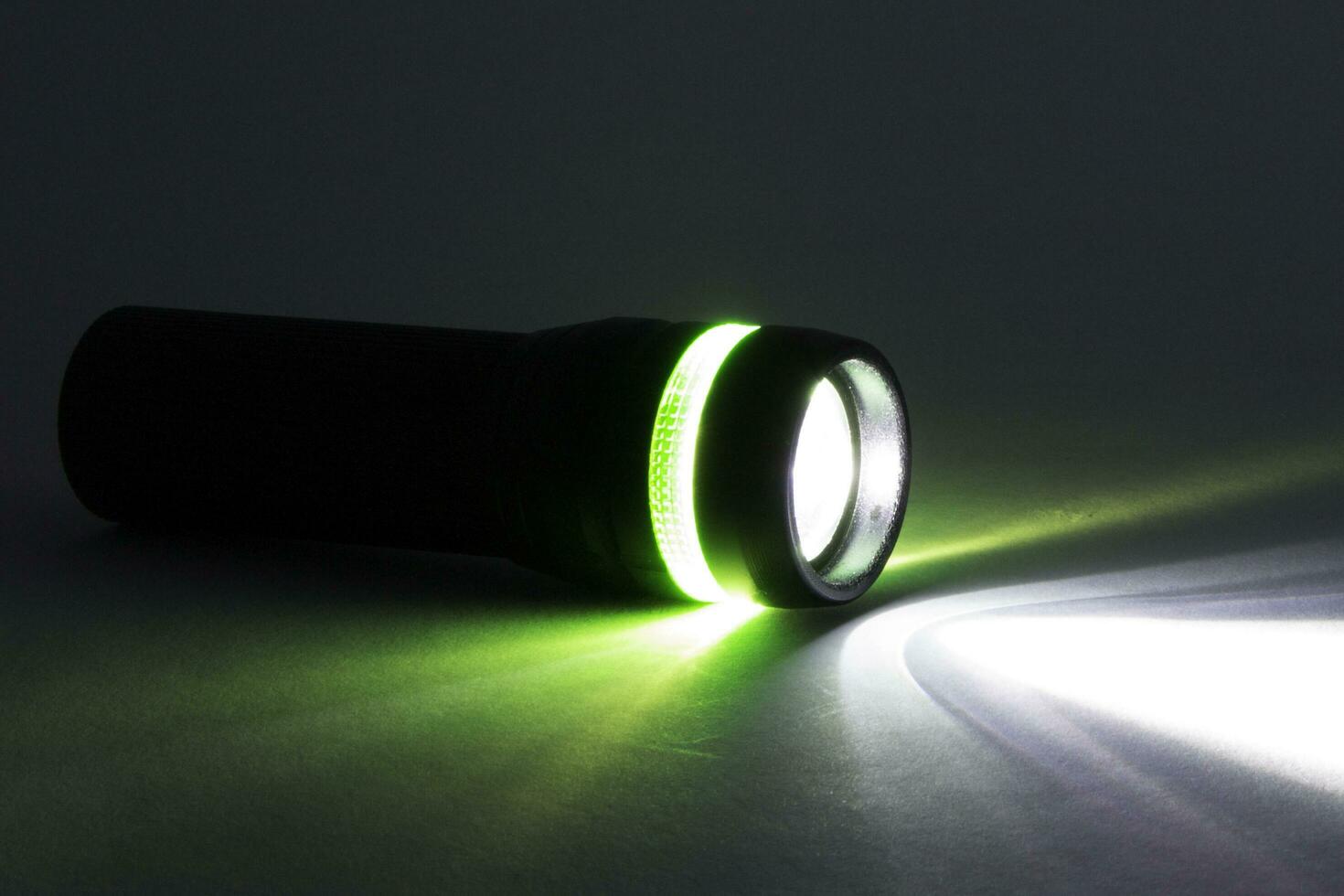 black flashlight lighting up shines green and white ray light beam torch. object emergency electric tool energy lamp lantern led battery power for security search or direction view finding in dark. photo