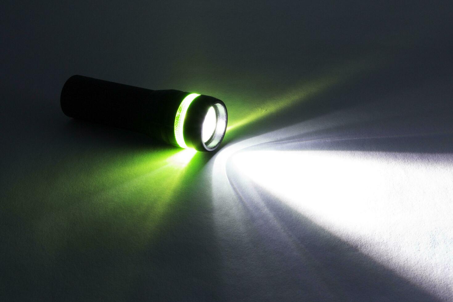 black flashlight lighting up shines green and white ray light beam torch. object emergency electric tool energy lamp lantern led battery power for security search or direction view finding in dark. photo