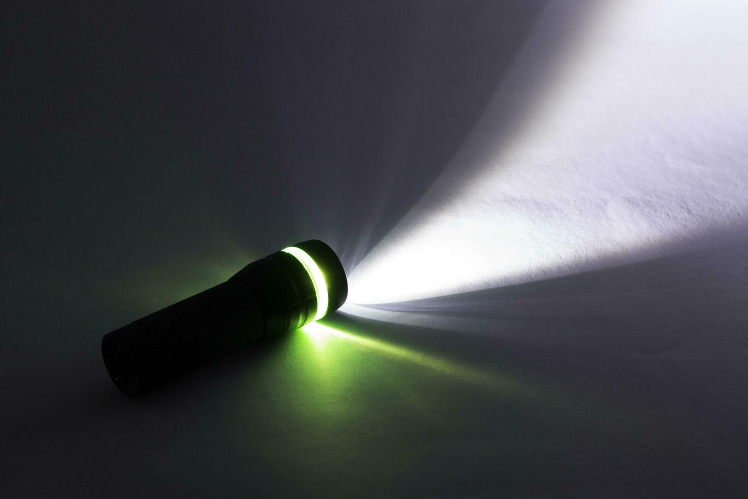 black flashlight lighting up shines green and white ray light beam torch. object emergency electric tool energy lamp lantern led battery power for security search or direction view finding in dark. photo