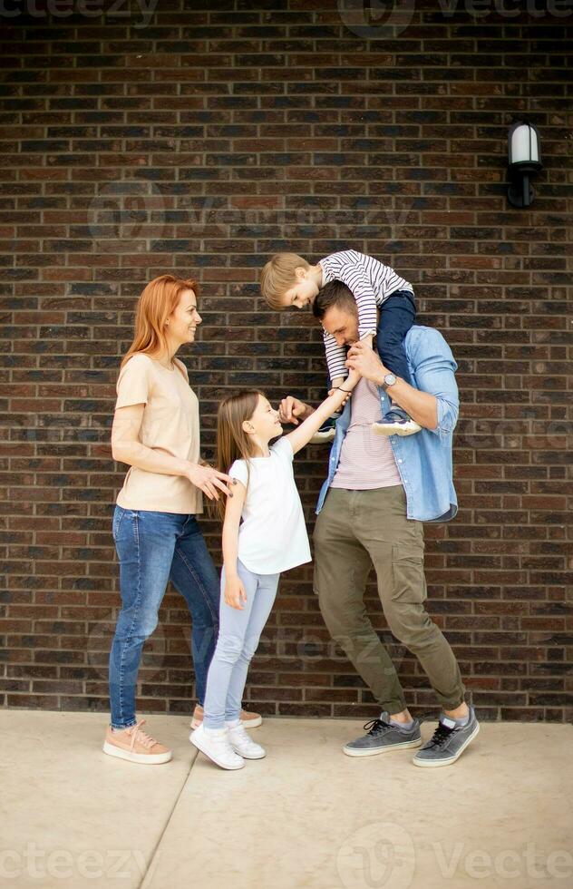 Family with a mother, father, son and daughter standing by the wall of brick house photo