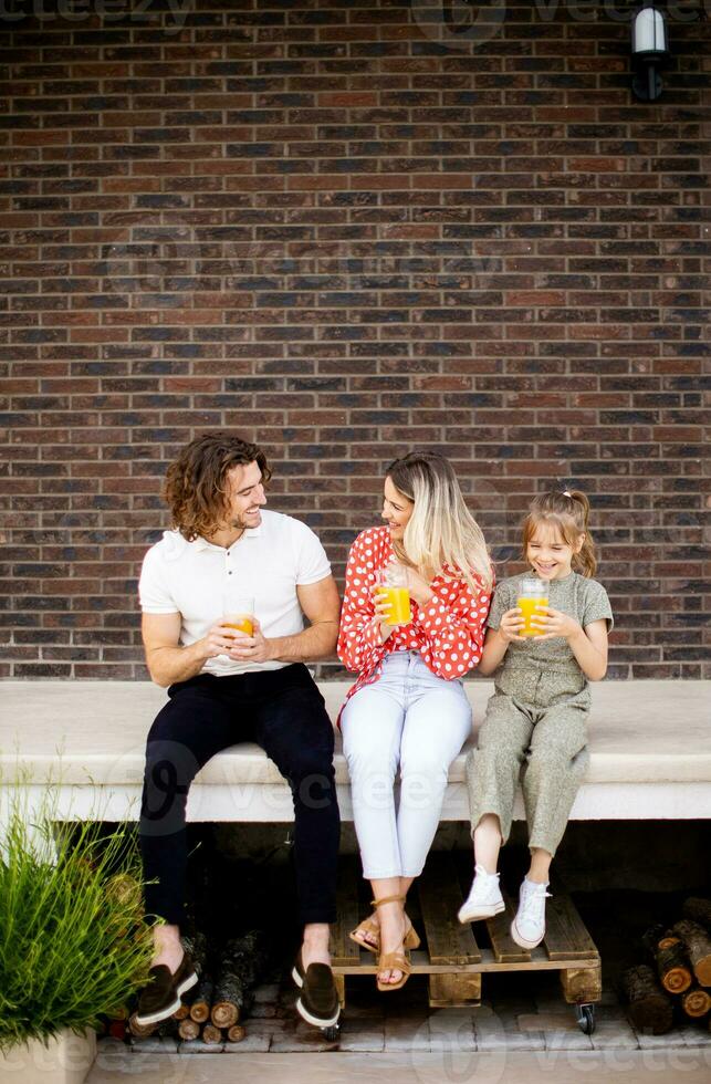 Family with a mother, father and daughter sitting outside on the steps of a front porch of a brick house photo