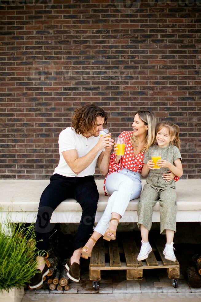 Family with a mother, father and daughter sitting outside on the steps of a front porch of a brick house photo