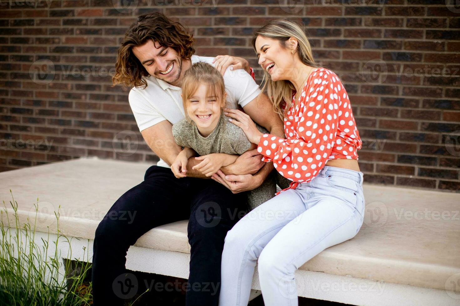 Family with a mother, father and daughter sitting outside on the steps of a front porch of a brick house photo