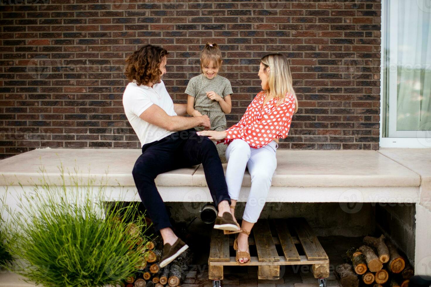 Family with a mother, father and daughter sitting outside on the steps of a front porch of a brick house photo