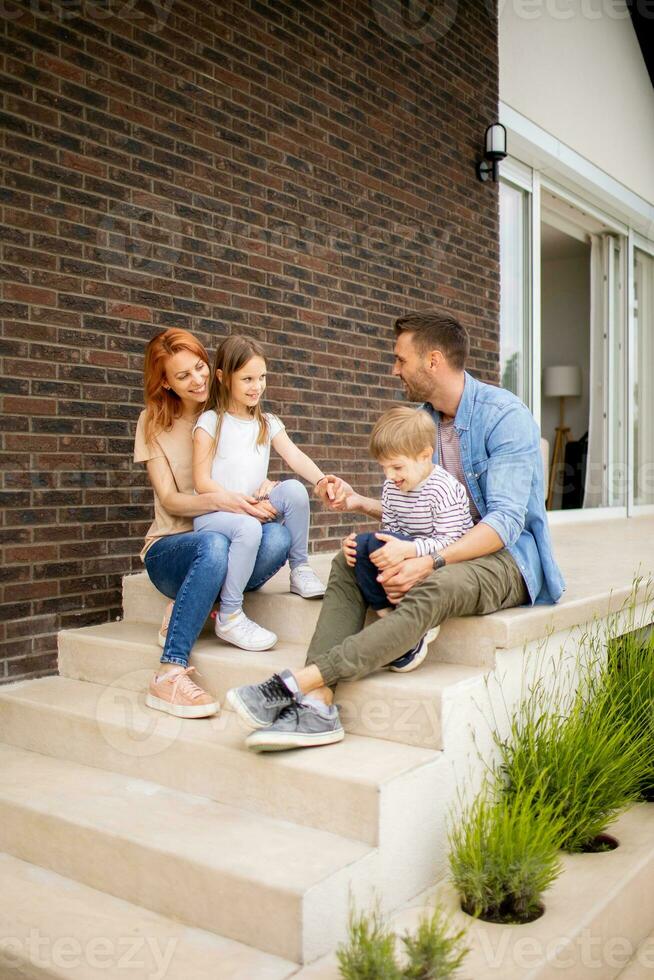 Family with a mother, father, son and daughter sitting outside on the steps of a front porch of a brick house photo