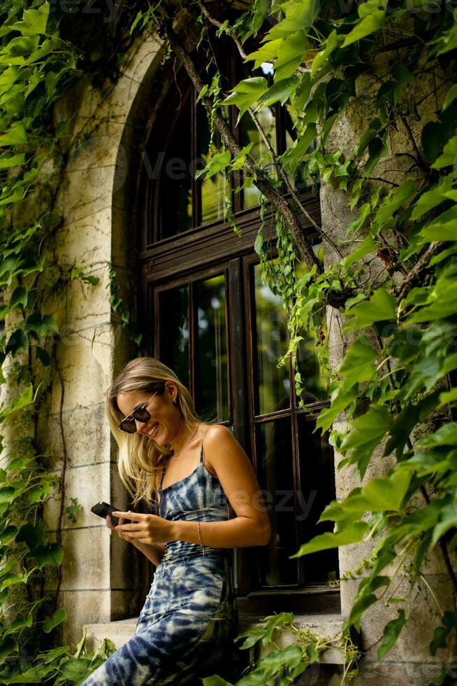 Pretty young woman using mobile phone by the old house with ivy photo