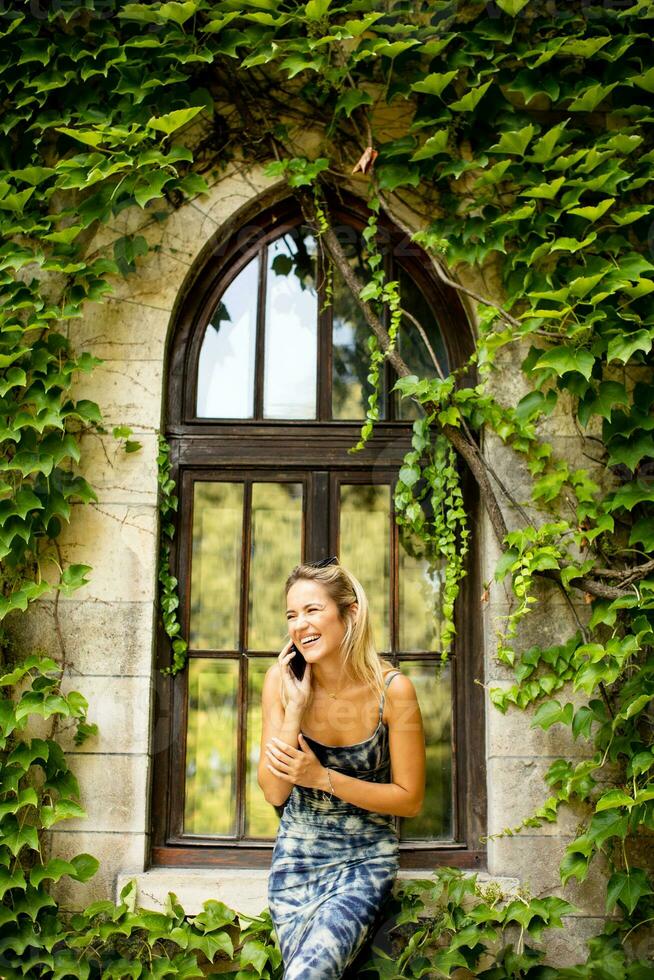 Pretty young woman using mobile phone by the old house with ivy photo