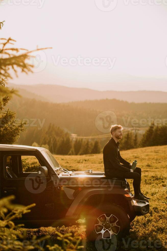 Young man relaxing on a terrain vehicle hood at countryside photo