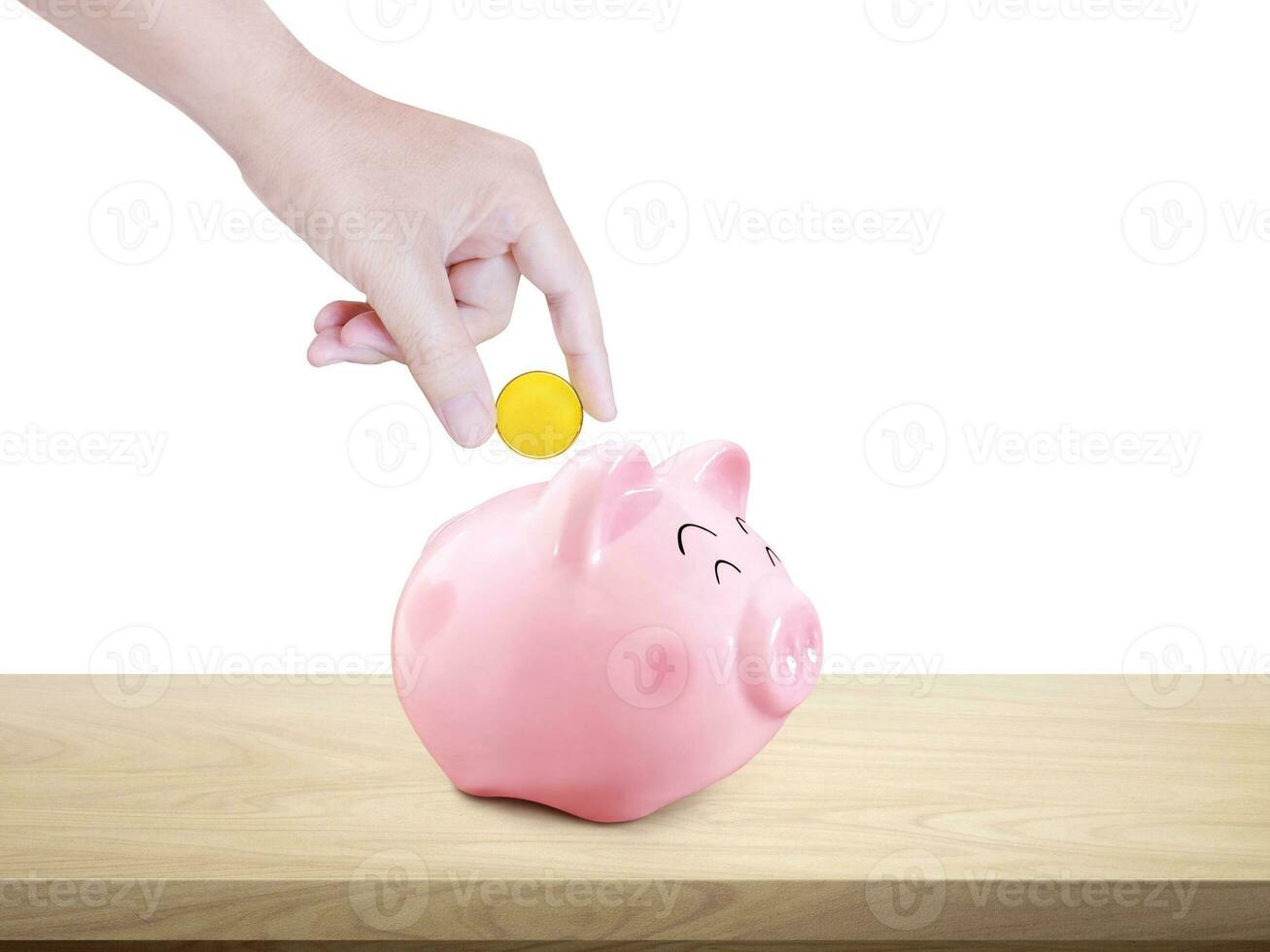 Hand puts gold coins into piggy bank on wooden table photo