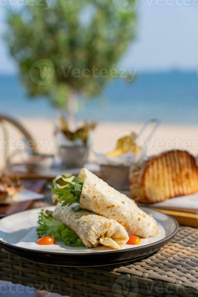 Spaghetti, pizza, french fries, beef steak on a wooden plate on the beach photo