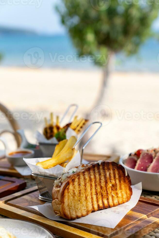 Spaghetti, pizza, french fries, beef steak on a wooden plate on the beach photo
