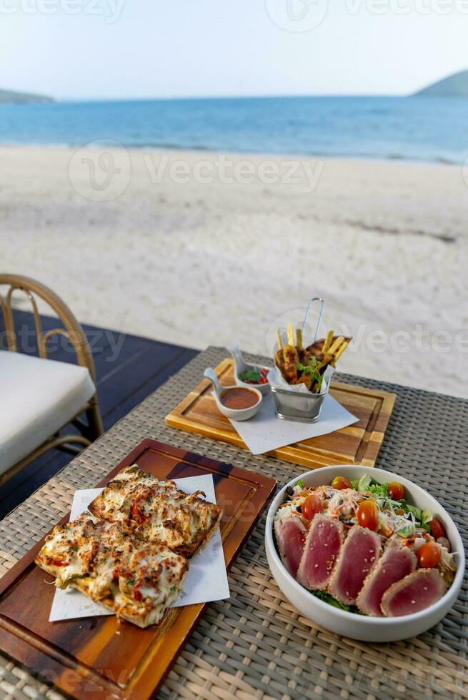 Spaghetti, pizza, french fries, beef steak on a wooden plate on the beach photo