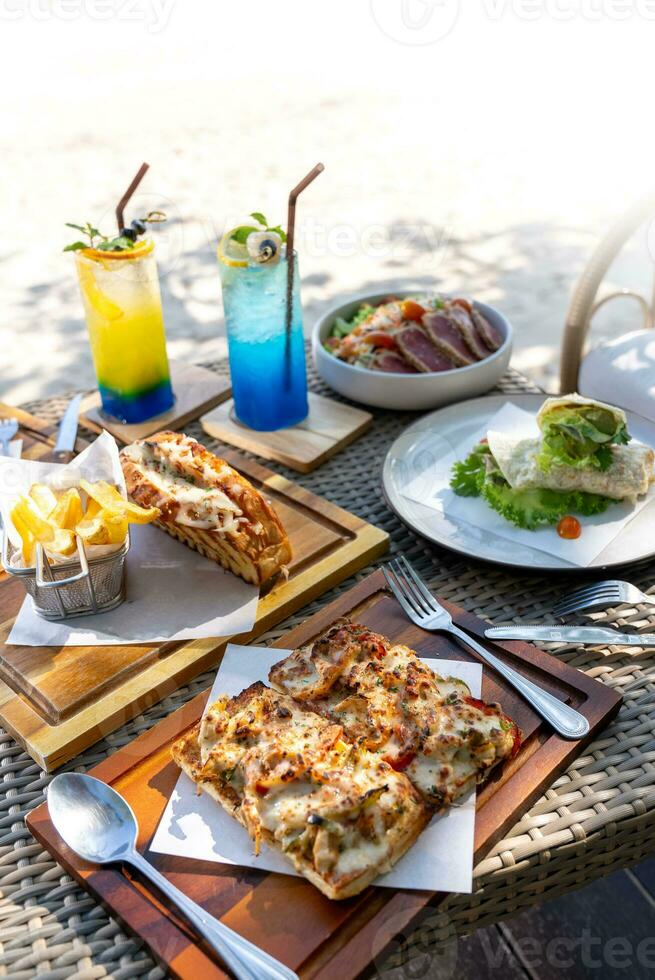 Spaghetti, pizza, french fries, beef steak on a wooden plate on the beach photo