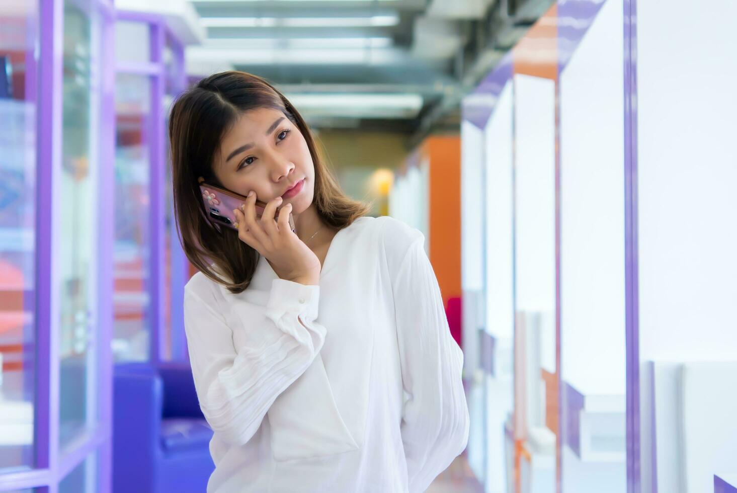 Beautiful asian business woman is standing and talking on the phone with a passive expression while looking at the copy space and communicating with her customers, Digital marketing. photo