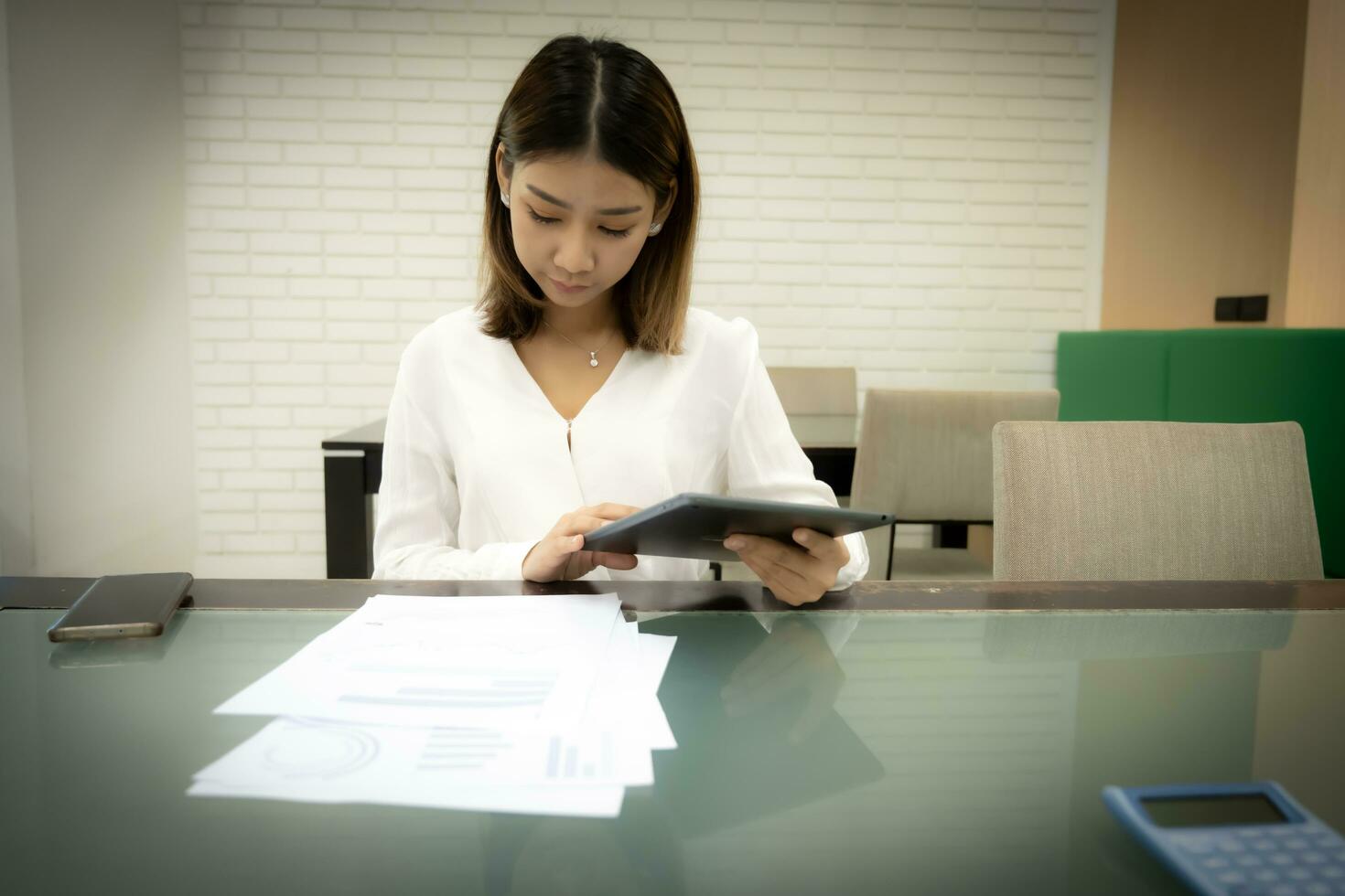 Beautiful asian business woman sitting examining documents about the company's finances while holding tablet with serious face. photo