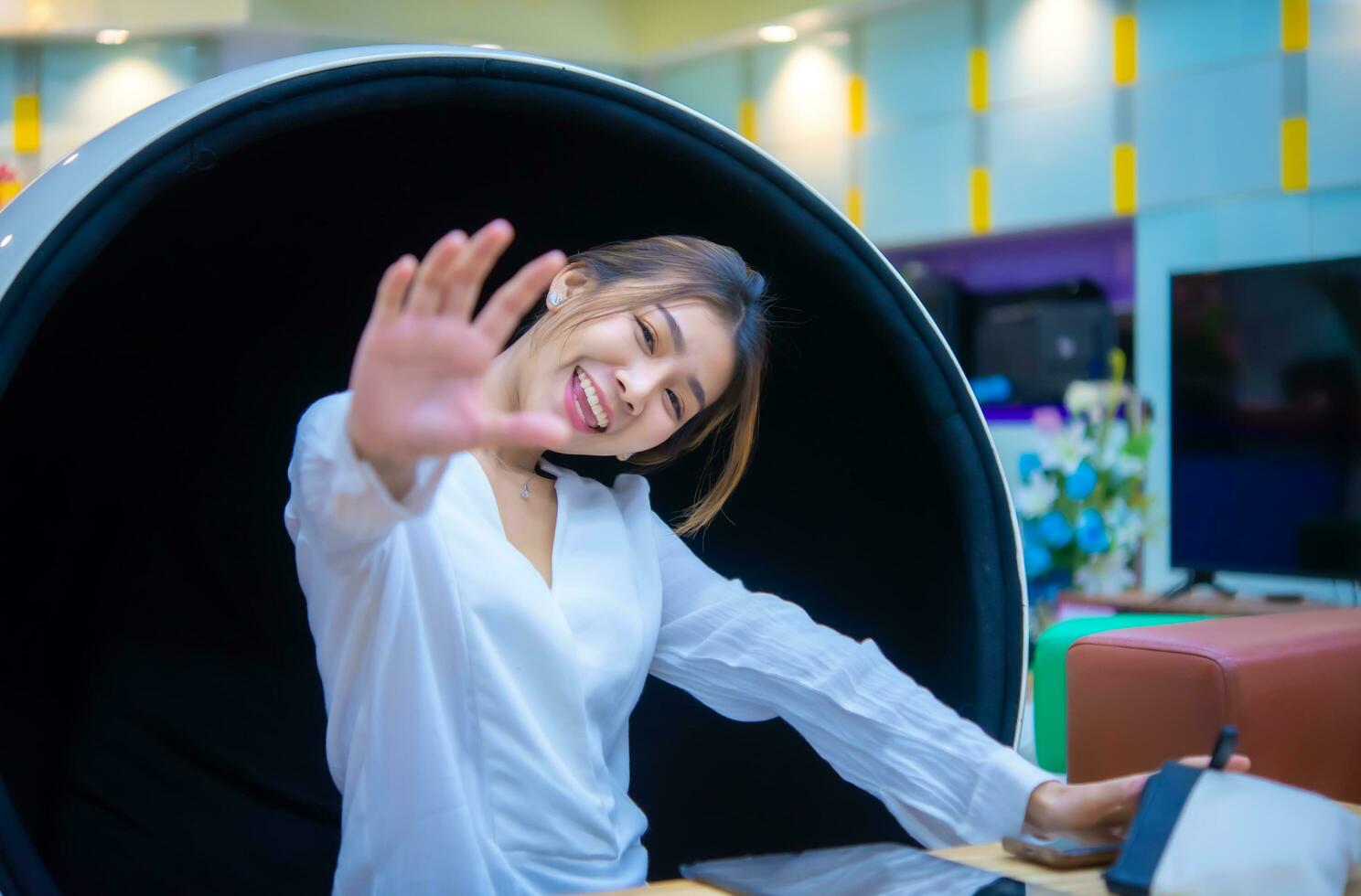 Beautiful asian business woman sitting on a modern round chair smiling at the camera her hand in front of while looking to the camera, Digital marketing. photo