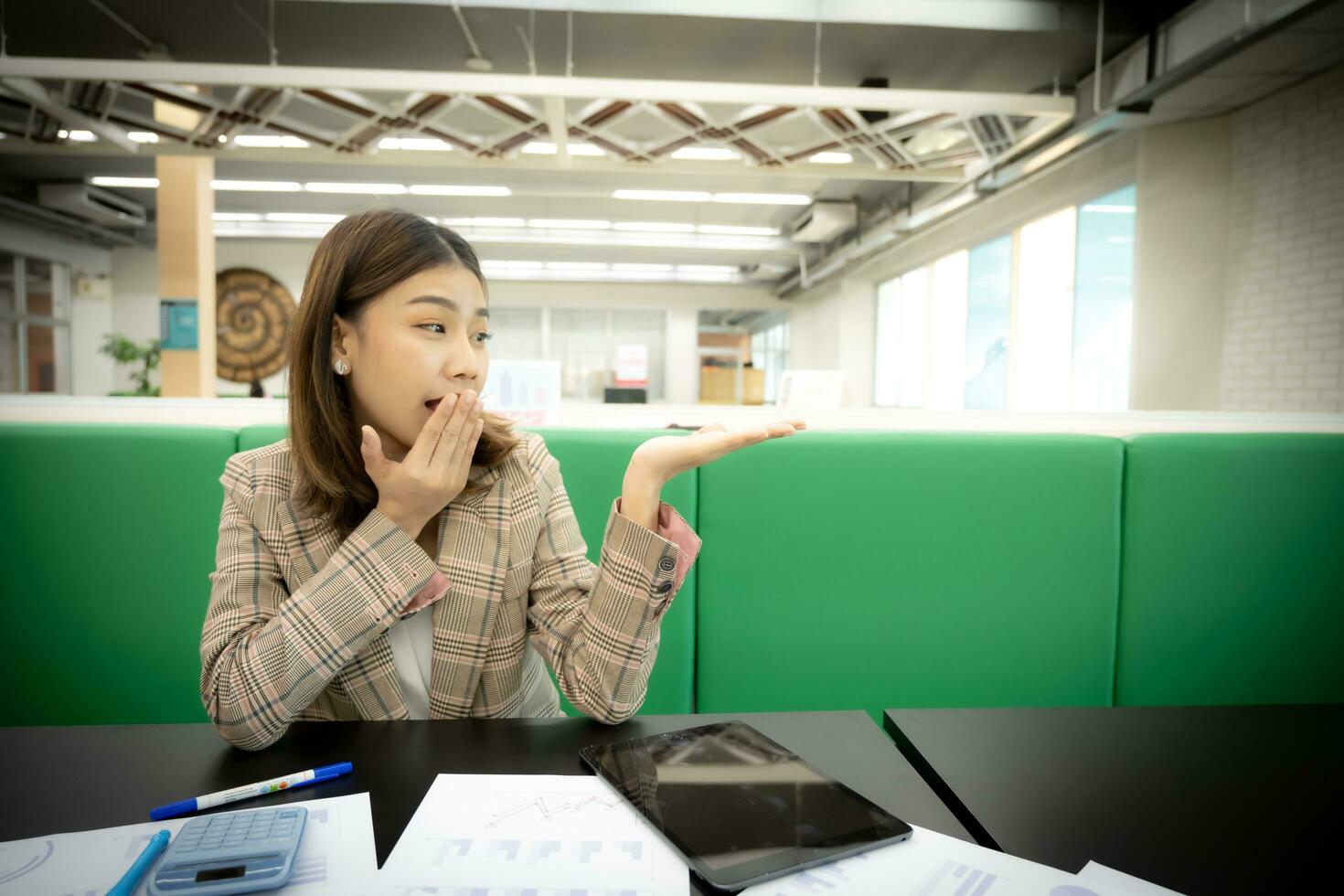 Beautiful asian businesswoman looks at the open hand with copy space with a surprised expression in her office. photo