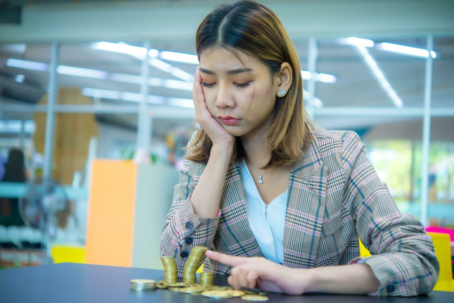 Pretty asian business woman touching with her fingers and looking at piles of crumbling gold coins with a sad expression. It conveys the mismanagement of financial management. photo