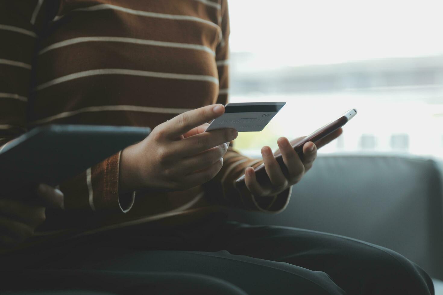 un crédito tarjeta en el manos de un joven mujer de negocios paga para un negocio en un móvil teléfono y en un escritorio con un ordenador portátil. foto