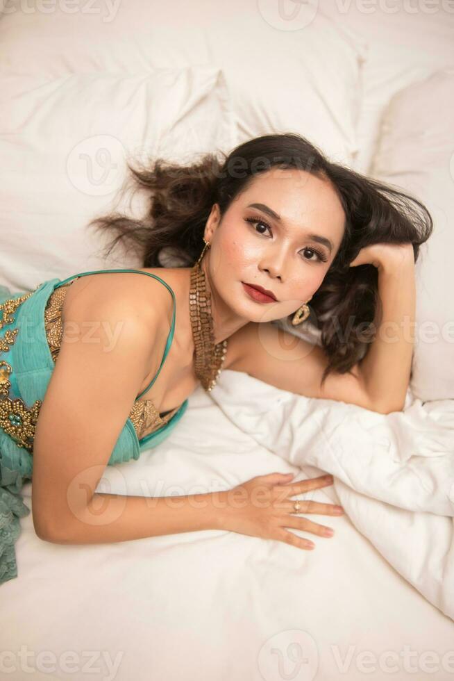 an Asian woman in a green dress is sleeping on a white bed in a luxury hotel photo
