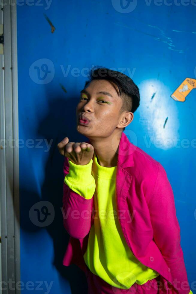 a gay Asian man posing very funny and humorous while wearing a pink suit in front of a blue background photo