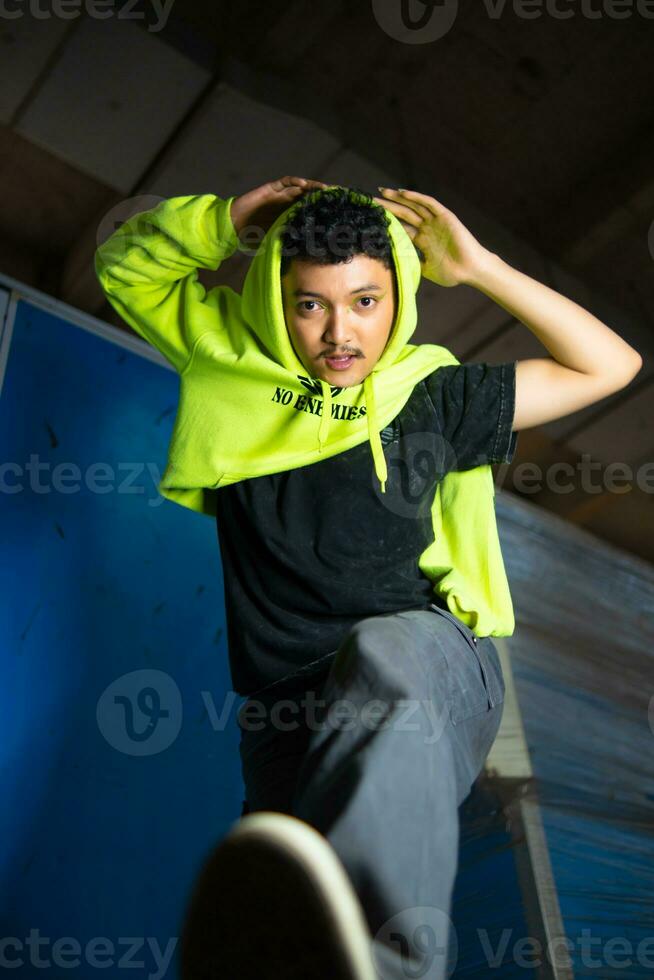 an Asian man with black curly hair posing in a green hoodie photo