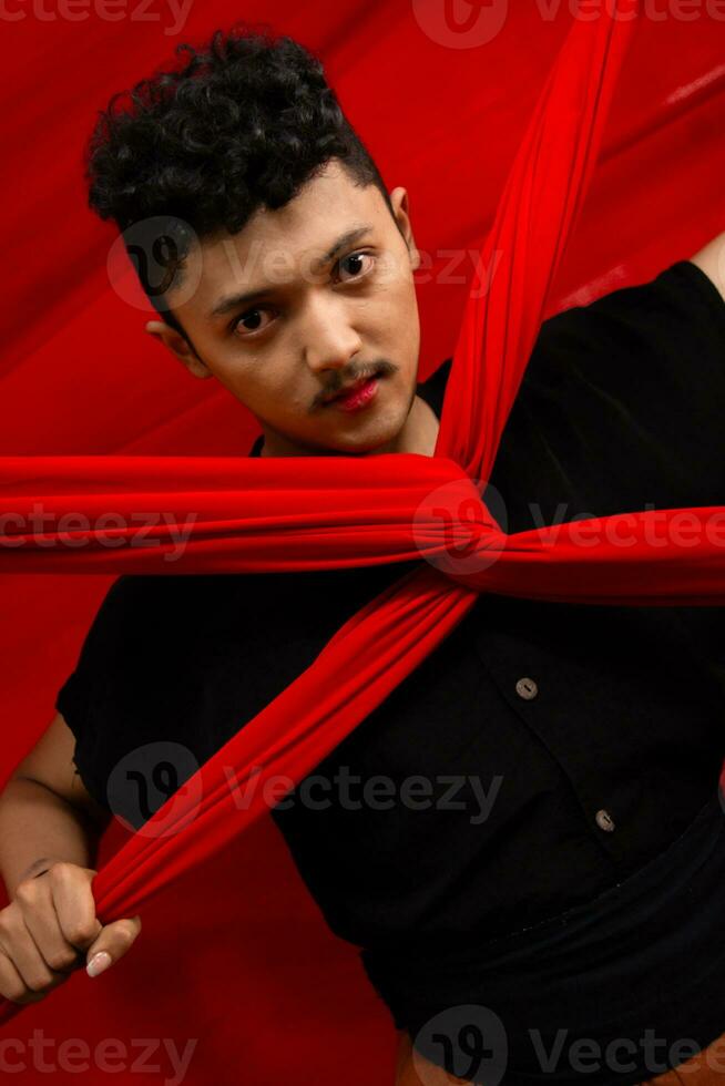 an Asian man stands in front of a red x-shaped cloth and holds it with both hands photo