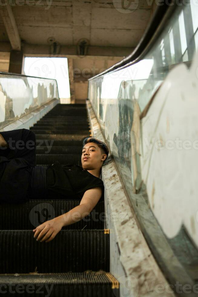 an Asian man in black clothes is sitting in a broken and abandoned elevator in an old building photo