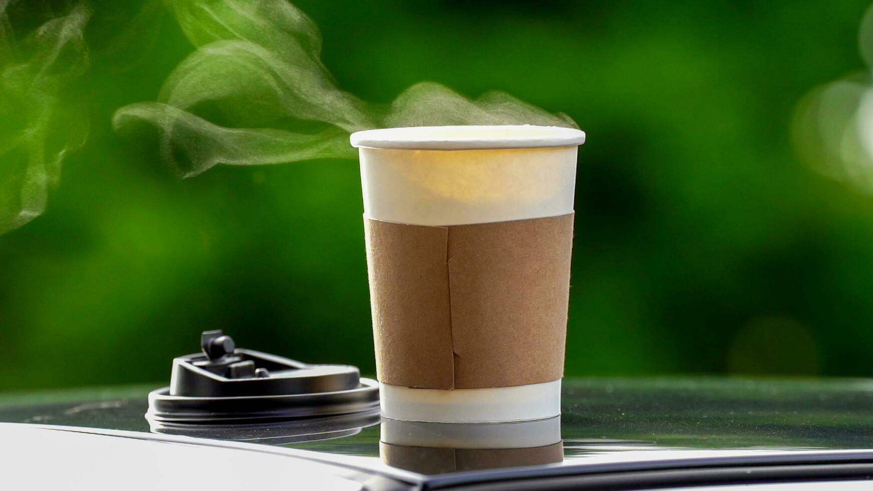 coffee takeaway in a paper cup on top of the car roof green tree background at sunrise in the morning,  selective focus, soft focus. photo