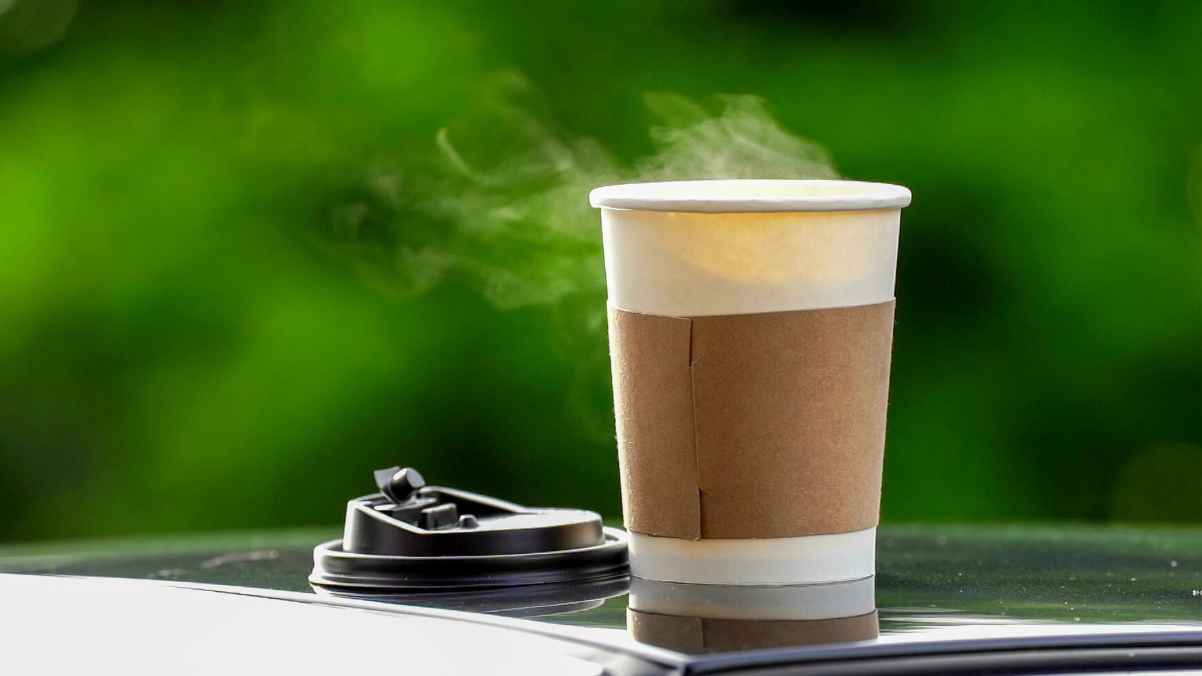 coffee takeaway in a paper cup on top of the car roof green tree background at sunrise in the morning,  selective focus, soft focus. photo