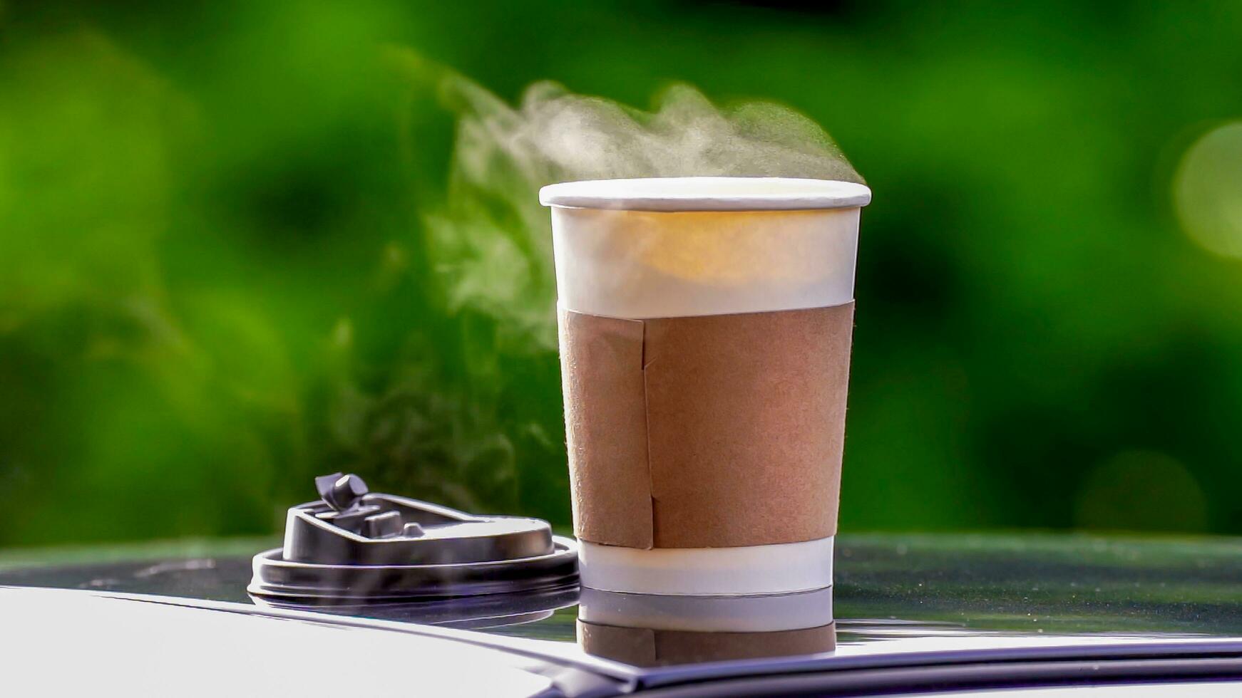 café para llevar en un papel taza en parte superior de el coche techo verde árbol antecedentes a amanecer en el mañana, selectivo enfocar, suave enfocar. foto