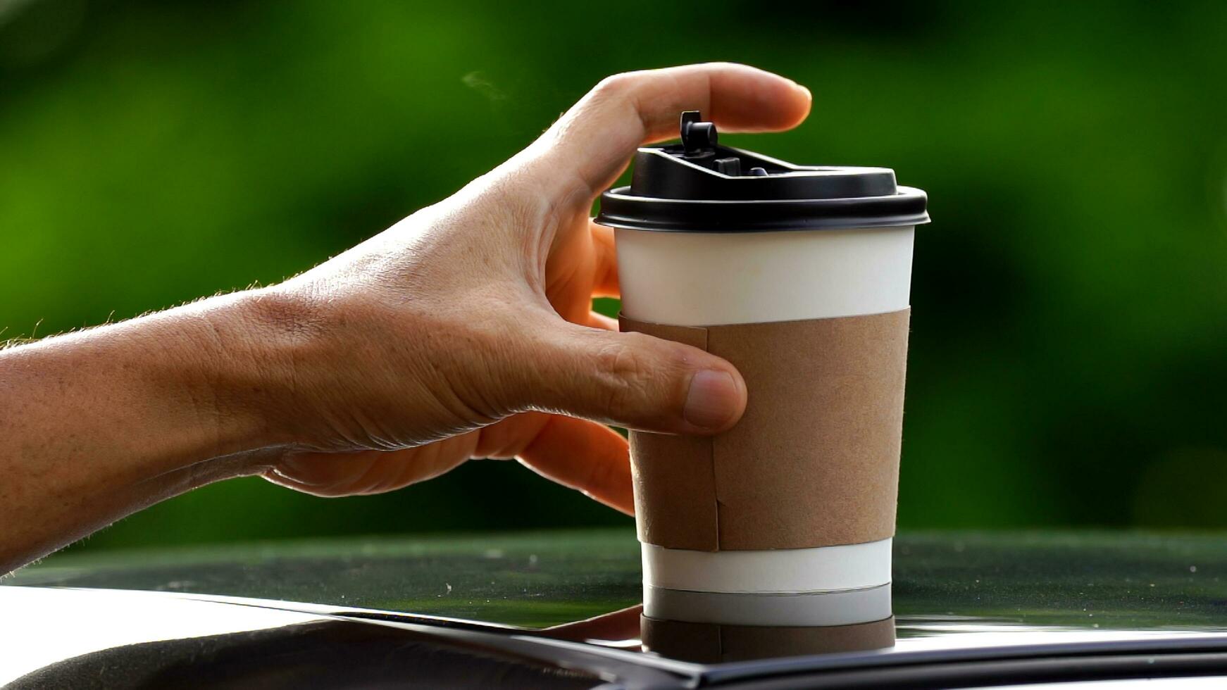 coffee takeaway in a paper cup on top of the car roof green tree background at sunrise in the morning,  selective focus, soft focus. photo