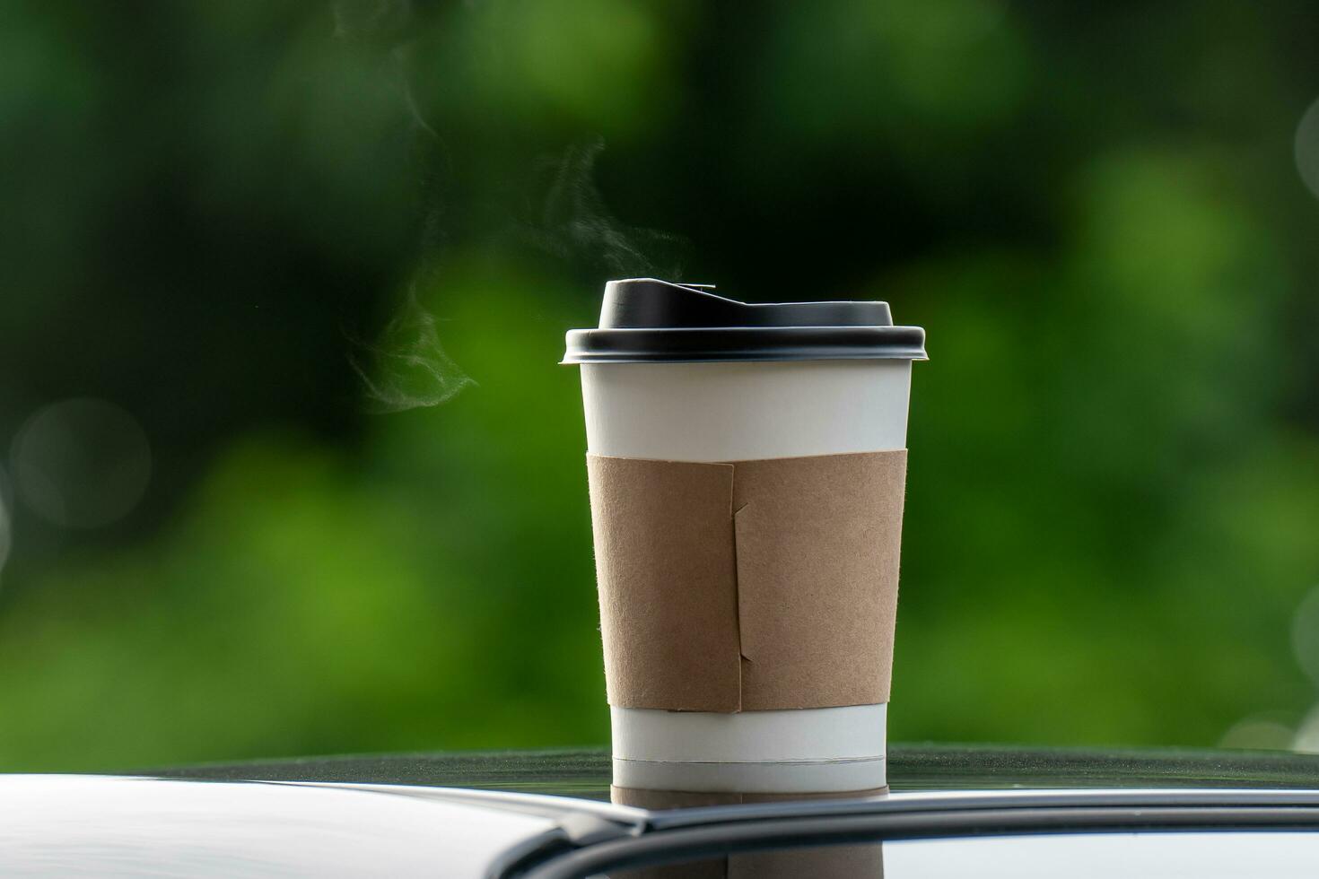 café para llevar en un papel taza en parte superior de el coche techo verde árbol antecedentes a amanecer en el mañana, selectivo enfocar, suave enfocar. foto