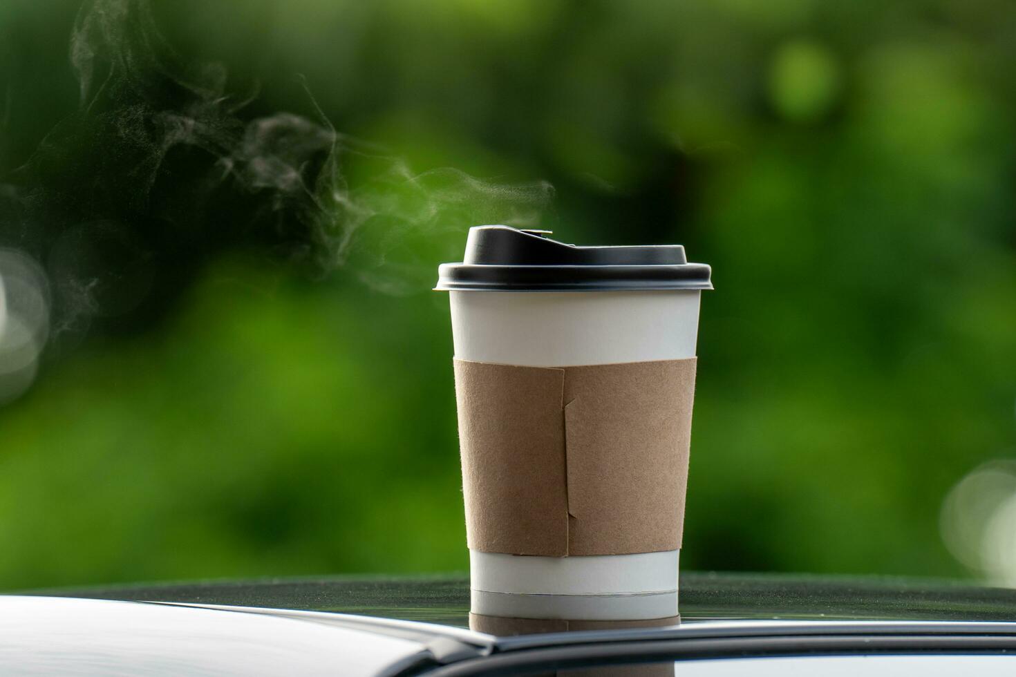 café para llevar en un papel taza en parte superior de el coche techo verde árbol antecedentes a amanecer en el mañana, selectivo enfocar, suave enfocar. foto