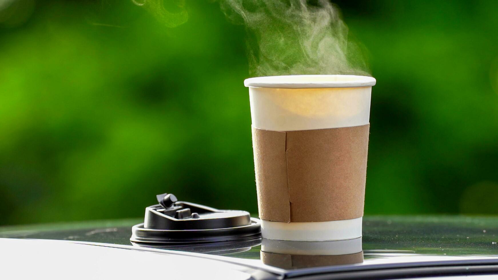 café para llevar en un papel taza en parte superior de el coche techo verde árbol antecedentes a amanecer en el mañana, selectivo enfocar, suave enfocar. foto