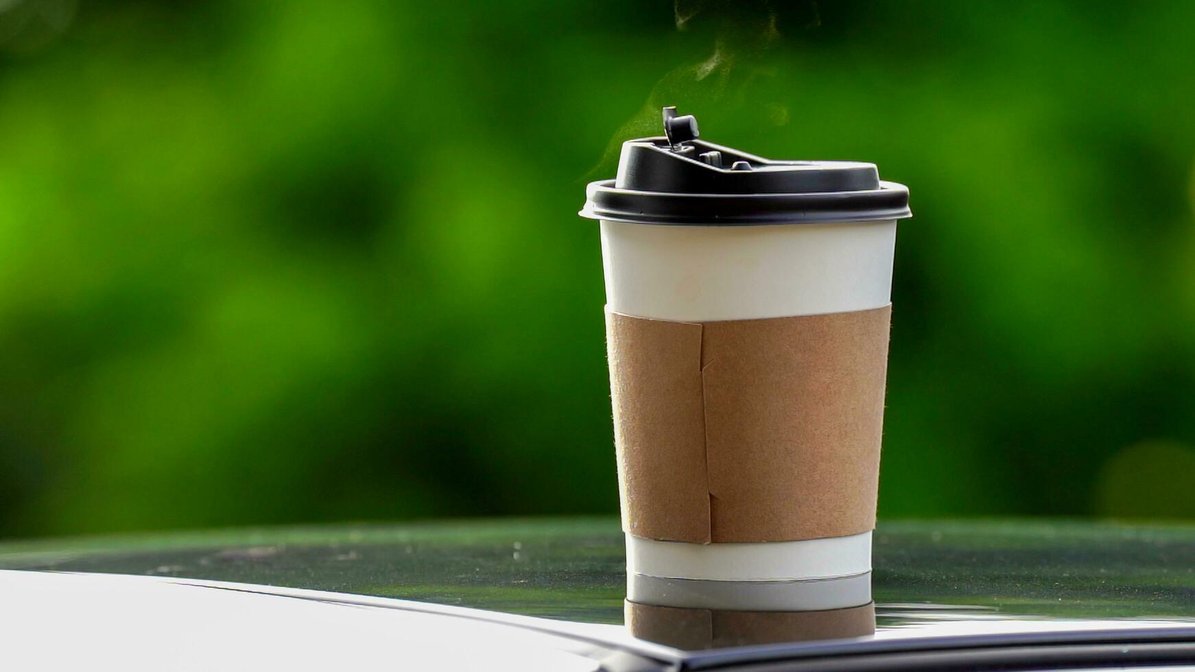 café para llevar en un papel taza en parte superior de el coche techo verde árbol antecedentes a amanecer en el mañana, selectivo enfocar, suave enfocar. foto