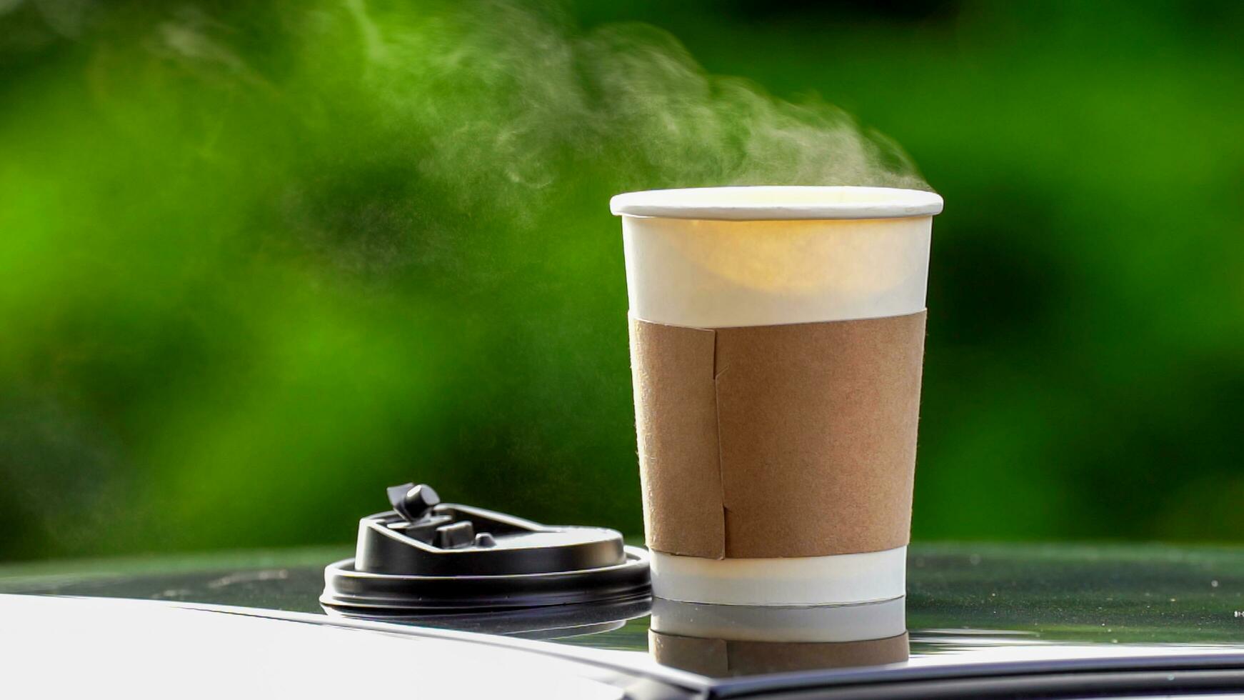 café para llevar en un papel taza en parte superior de el coche techo verde árbol antecedentes a amanecer en el mañana, selectivo enfocar, suave enfocar. foto