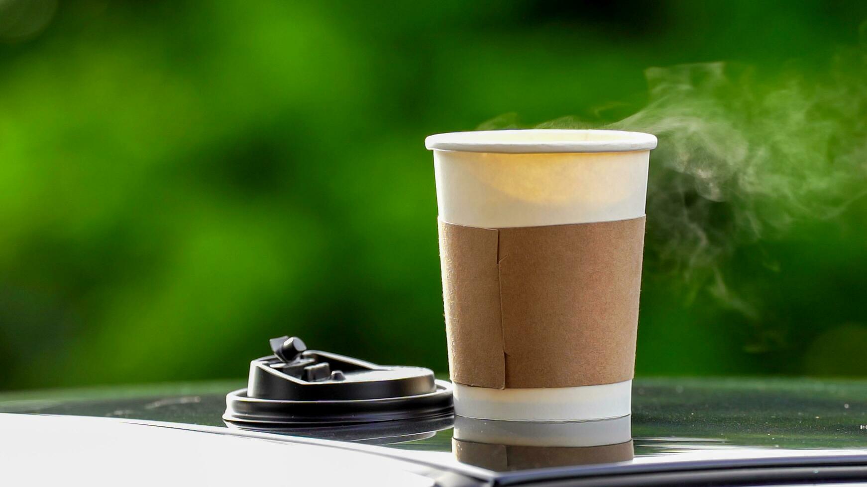 coffee takeaway in a paper cup on top of the car roof green tree background at sunrise in the morning,  selective focus, soft focus. photo