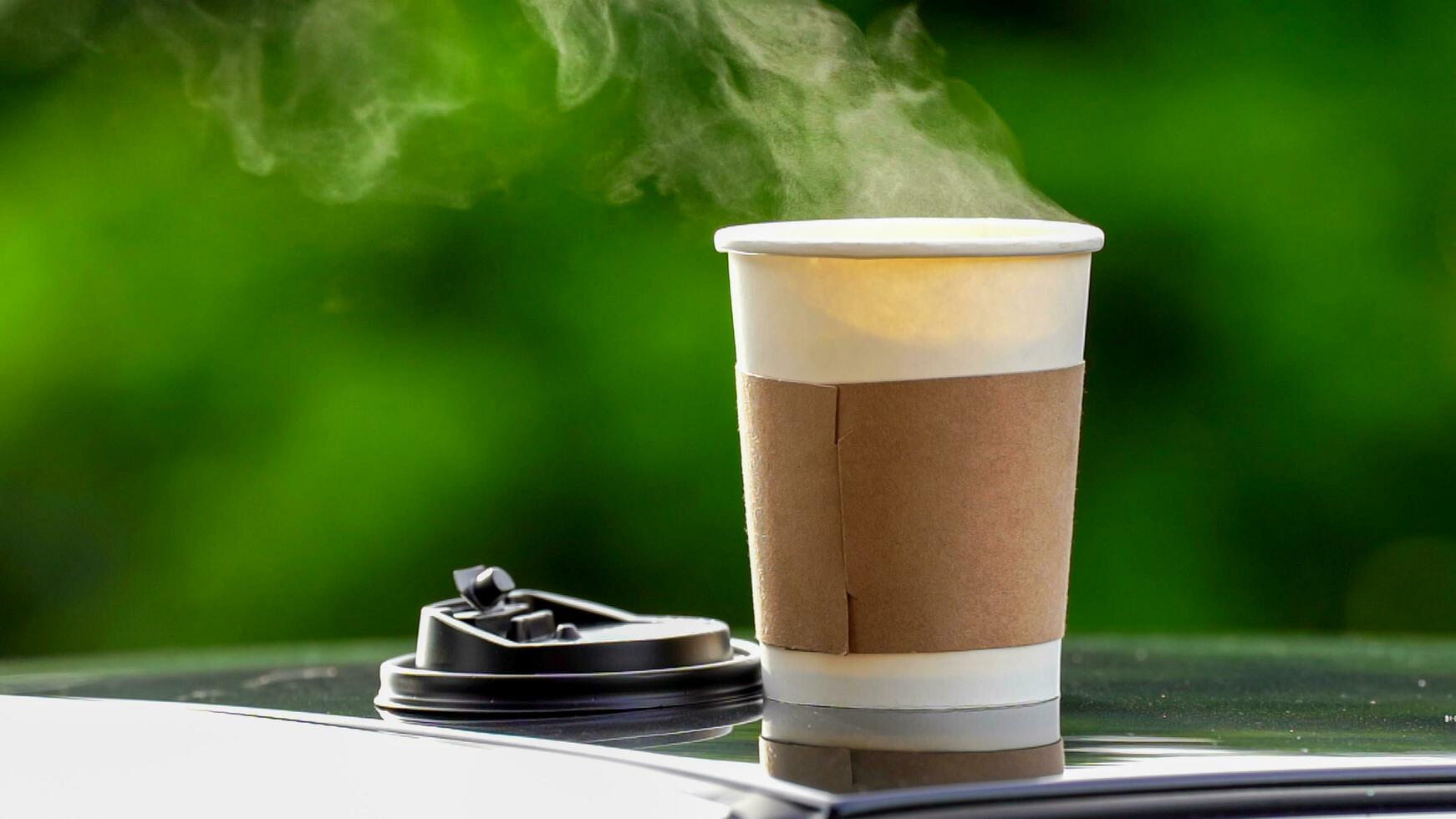 café para llevar en un papel taza en parte superior de el coche techo verde árbol antecedentes a amanecer en el mañana, selectivo enfocar, suave enfocar. foto