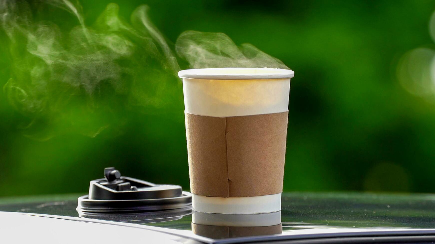 café para llevar en un papel taza en parte superior de el coche techo verde árbol antecedentes a amanecer en el mañana, selectivo enfocar, suave enfocar. foto