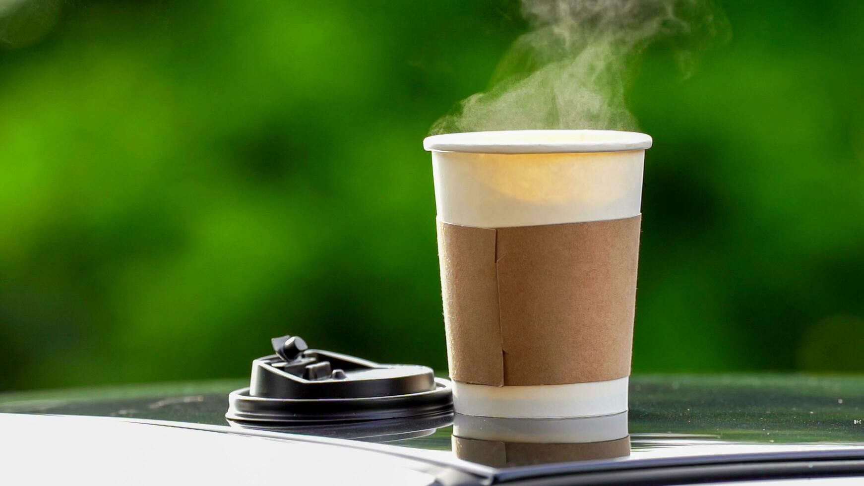 café para llevar en un papel taza en parte superior de el coche techo verde árbol antecedentes a amanecer en el mañana, selectivo enfocar, suave enfocar. foto