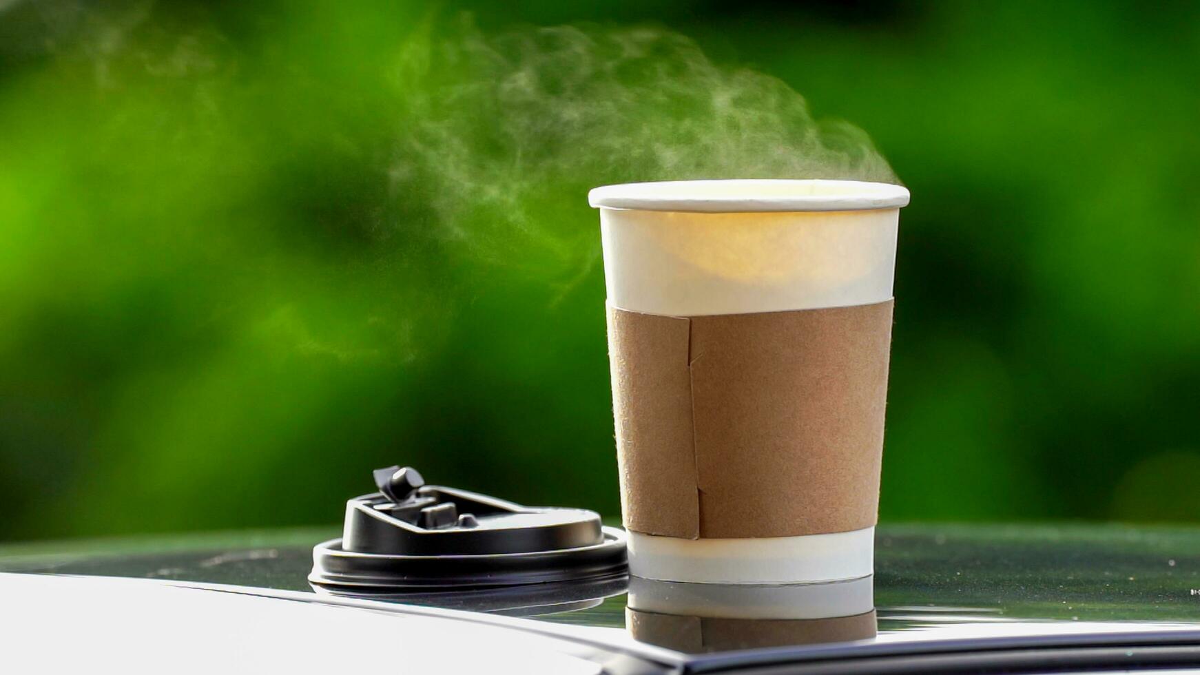 coffee takeaway in a paper cup on top of the car roof green tree background at sunrise in the morning,  selective focus, soft focus. photo