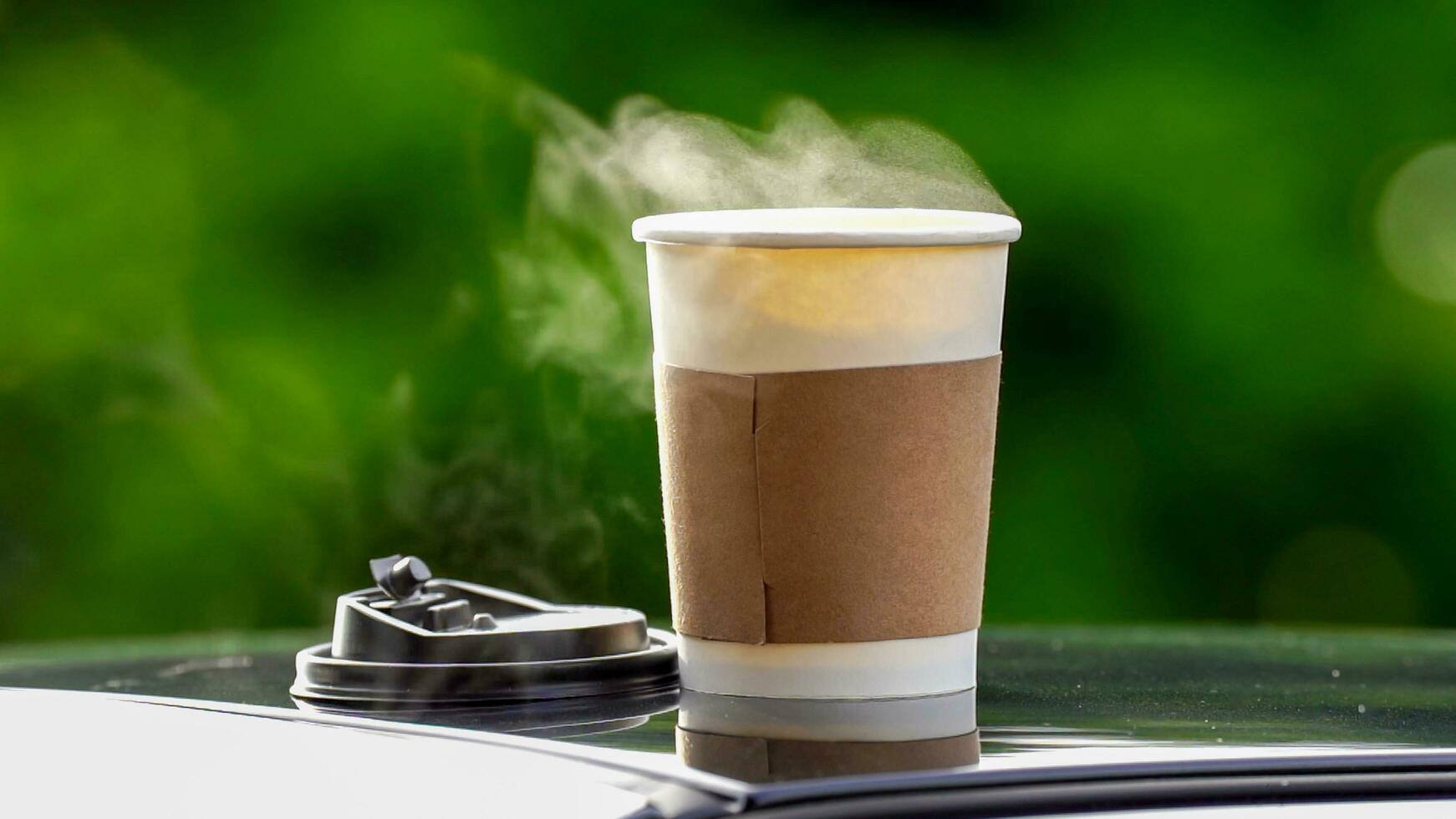 coffee takeaway in a paper cup on top of the car roof green tree background at sunrise in the morning,  selective focus, soft focus. photo