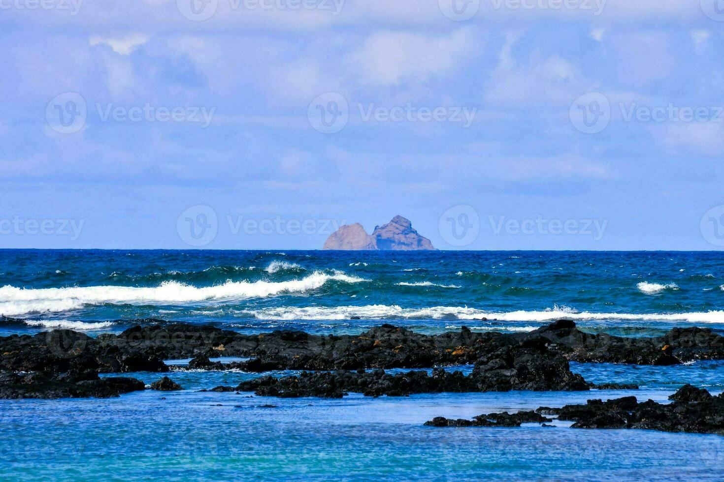 a view of the ocean and rocks with a small island in the distance photo