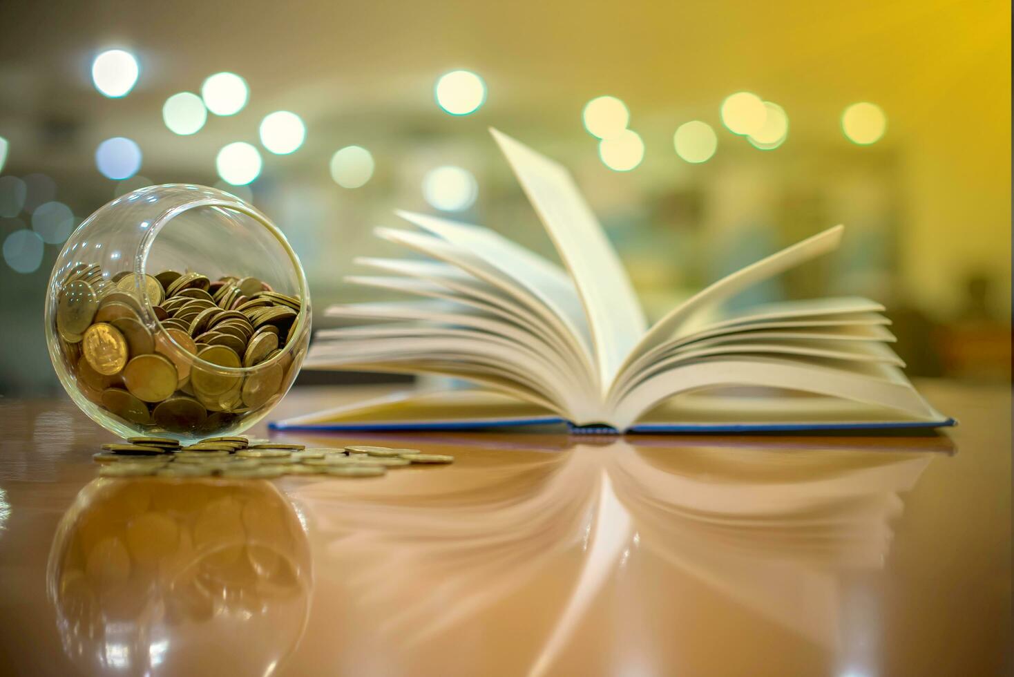 Money coins Thai baht in a round glass jar with a book is opening and Bokeh background. Banking, Finance and Saving money concept. photo