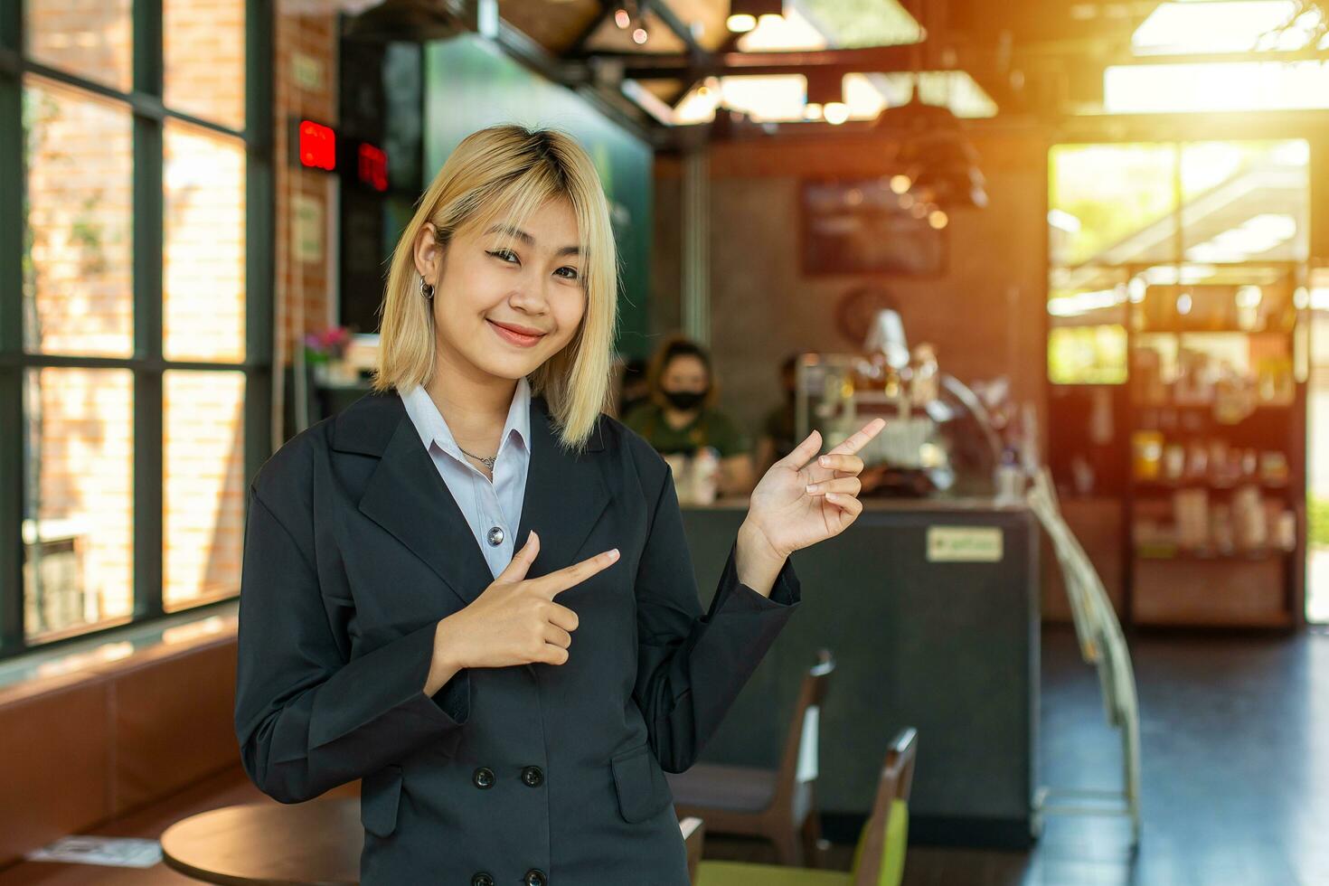 With a proud smile, the beautiful business girl pointed to her cafe and enthusiastically invited passersby to come in and check it out. photo