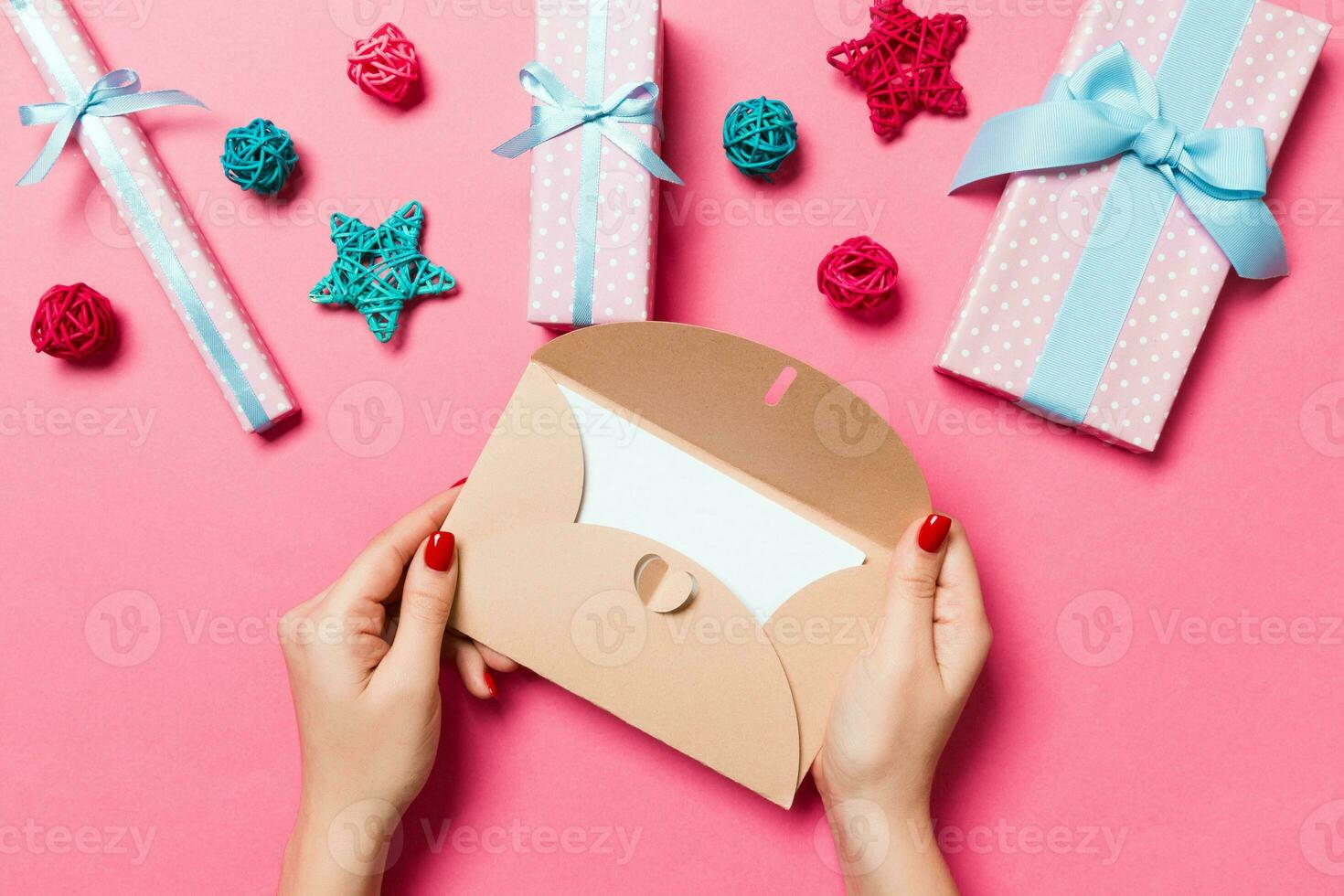 Top view of woman holding an envelope on pink background made of holiday decorations. Christmas time concept photo