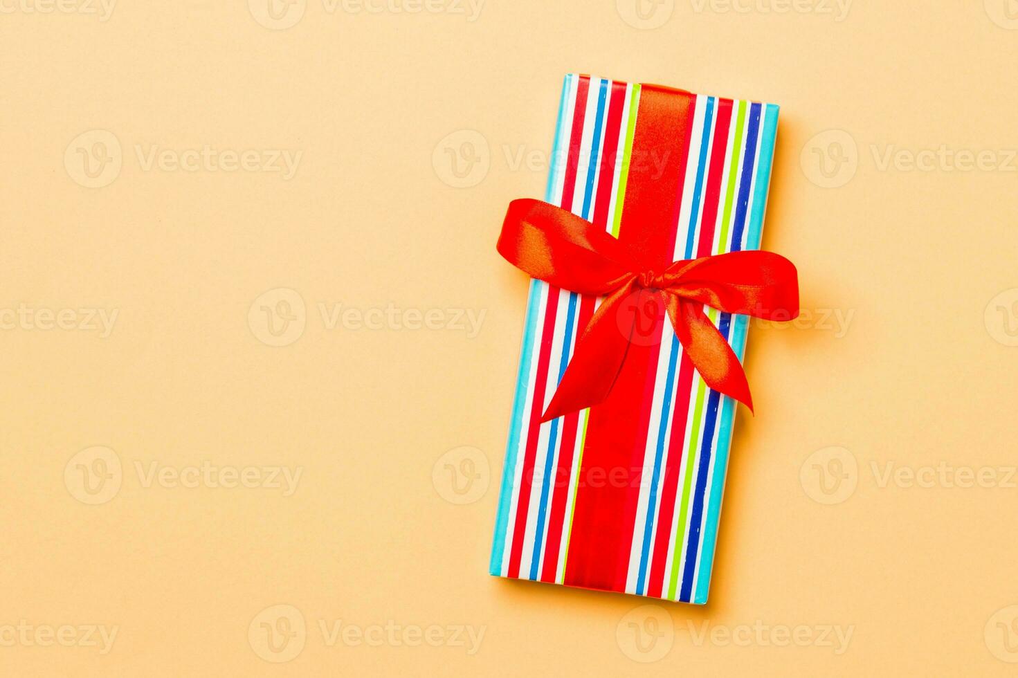 Top view Christmas present box with red bow on orange background with copy space photo