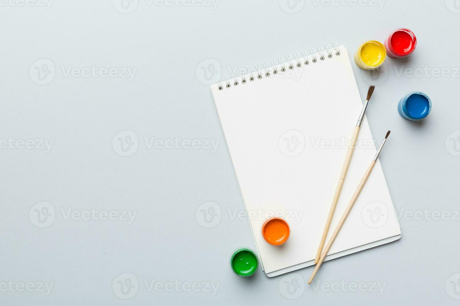 Album pages and paints, pencils, brush on a colored background. Top view with empty space. workplace for creativity. home teaching concept drawing photo